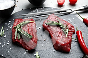 Fresh raw meat steaks and spices on slate plate, closeup