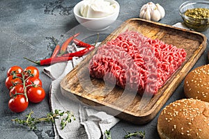 Fresh raw minced beef steak burgers with spices ingredients, on wooden tray, on gray stone background