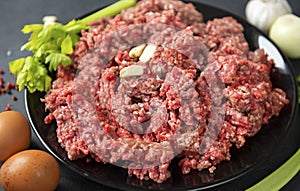 Fresh raw minced meat with garlic cloves on a black plate