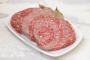 fresh raw minced meat on white dish with bay leaf