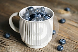 Fresh raw organic farm blueberry in white cup on rustic wooden background.