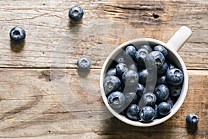 Fresh raw organic farm blueberry in white cup on rustic wooden background.