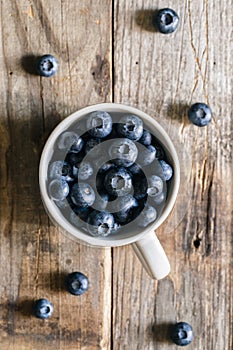 Fresh raw organic farm blueberry in white cup on rustic wooden background.