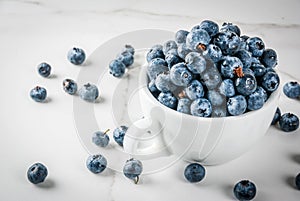 Fresh raw organic farm blueberry in white cup on white marble kitchen background, copy space