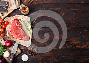 Fresh raw organic slice of braising steak fillet on butchers paper with fork and knife on dark wooden background. Red onion,