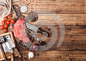 Fresh raw organic slice of braising steak fillet on chopping board with fork and knife on wooden background. Red onion, tomatoes