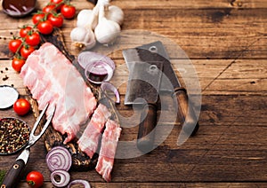 Fresh raw pieces of pork ribs on chopping board and vintage meat hatchets on wooden background. Fresh tomatoes and red onion with