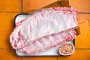 Fresh Raw pork spare loin ribs in a steel tray with herbs. Orange background. Top view