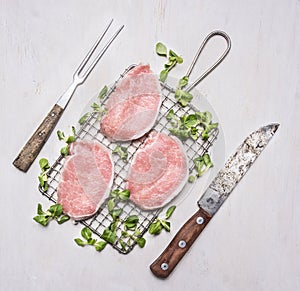 Fresh raw pork steaks with herbs, a knife and fork for the meat on the grill for roasting wooden rustic background top view