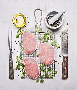 Fresh raw pork steaks with herbs, a knife and fork for the meat on the grill for roasting wooden rustic background top view