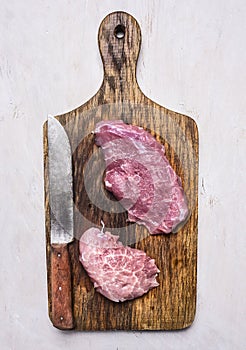 Fresh raw pork steaks with a knife for meat on vintage old cutting board a white background top view close up