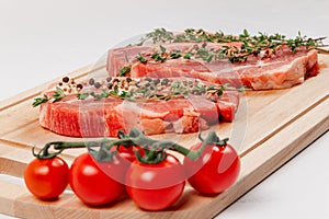 Fresh  raw pork steaks with spices, tomatoes and thyme on a cutting kitchen board on a white wooden table