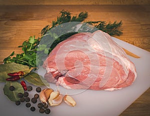 Fresh raw pork on wooden cutting board, spices and herbs. Whole uncooked pork prepare for cooking.