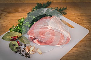 Fresh raw pork on wooden cutting board, spices and herbs. Whole uncooked pork prepare for cooking.
