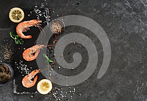 Fresh raw prawns or boiled red shrimps with spices and lemon on slate stone on dark stone background. Seafood, top view, flat lay