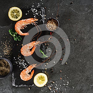 Fresh raw prawns or boiled red shrimps with spices and lemon on slate stone on dark stone background. Seafood, top view, flat lay