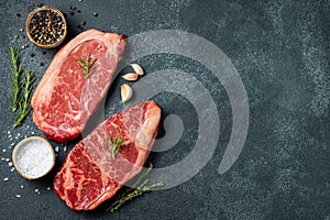 Fresh raw Prime Black Angus beef steaks on stone board: Striploin, Rib Eye. Top view with copy space. On a dark background