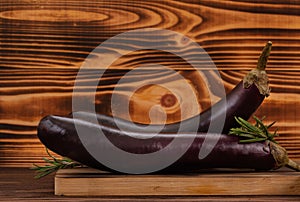 Fresh raw purple eggplants and rosemary leaves on brown wooden background