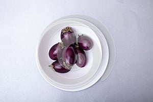 Fresh raw purple eggplants in a white eggplant plate on a gray background.