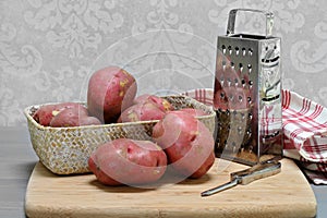 Fresh raw red potatoes in a basket on cutting board with utensils