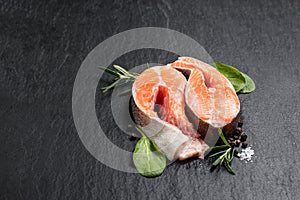 Fresh raw rianbow trout steaks with salt and spices on black stone background