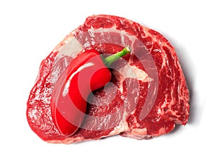 Fresh raw ribeye steak with one red chilly pepper. White isolated background,