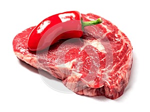 Fresh raw ribeye steak with one red chilly pepper. White isolated background