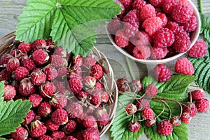 Fresh raw ripe strawberries with green leaves and a bowl of raspberries on old rustic wooden table .