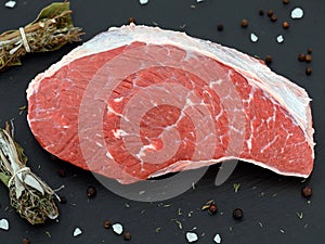 fresh raw rump meat cut from the picanha cap on a black slate plate with salt, pepper and bundle of spices