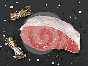 fresh raw rump meat cut from the picanha cap on a black slate plate with salt, pepper and bundle of spices