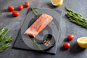 Fresh raw salmon fellet with pepper, salt, rosemary and lemon served on black stone board. Restaurant menu, healthy nutrition,