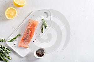 Fresh raw salmon fellet with pepper, salt, rosemary and lemon served on white stone board on white background. Restaurant menu,