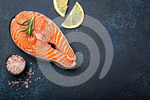 Fresh raw salmon fillet steak with rosemary on dark blue rustic stone background with rose salt and lemon top view