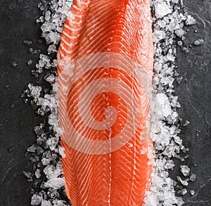 Fresh raw salmon fish steak with spices on ice over dark stone background. Creative layout made of fish, top view, flat lay