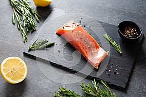 Fresh raw salmon red fish fillet with spieces, herbs and lemon ready for cooking on black background, side view. Restaurant menu,