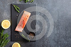 Fresh raw salmon red fish fillet with spieces, herbs and lemon ready for cooking on black background, top view. Restaurant menu,