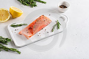 Fresh raw salmon red fish fillet with spieces, herbs, lemon and tomatoes on white background, side view. Restaurant menu, recipe.