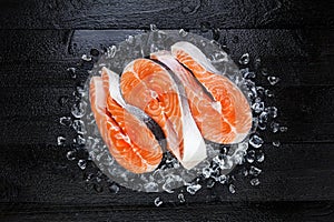 Fresh raw salmon red fish steak on ice on black wooden table top view