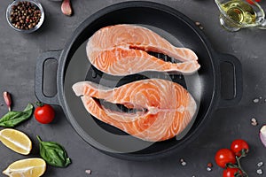 Fresh raw salmon steaks in a grill pan and ingredients on a dark background. Top view