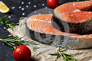 Fresh raw salmon steaks with salt, peppers, lemon, tomatoes and rosemary on the rustic paper