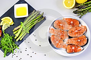 Fresh raw salmon steaks with vegetables and spices: asparagus, tomatoes, peppercorns, rucola, lemon and olive oil on gray backgrou