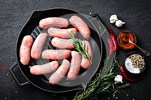 Fresh raw sausages on a cast-iron grill pan on a black background
