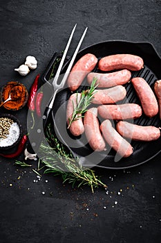 Fresh raw sausages on a cast-iron grill pan on a black background