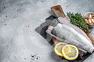 Fresh Raw Sea Bass fillets, Branzino fish with thyme and lemon. Gray background. Top view. Copy space