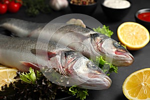 Fresh raw sea bass fish and ingredients on black table, closeup