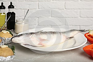 Fresh raw sea bass fish and ingredients on light gray marble table