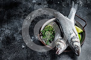 Fresh Raw Sea Bass, Labrax fish with herbs and lime. Black background. Top view. Copy space