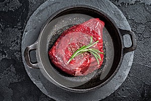 Fresh Raw sirloin rump steak in a skillet with herbs. Black background. Top view