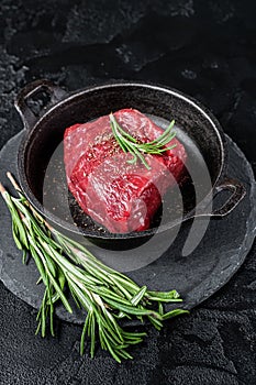 Fresh Raw sirloin rump steak in a skillet with herbs. Black background. Top view