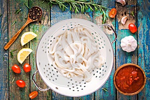 Fresh raw squid rings in a colander on a wooden table